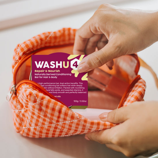 A close-up of a person's hands placing a purple Washu4 Repair & Nourish conditioning bar into an orange and white gingham zippered pouch.